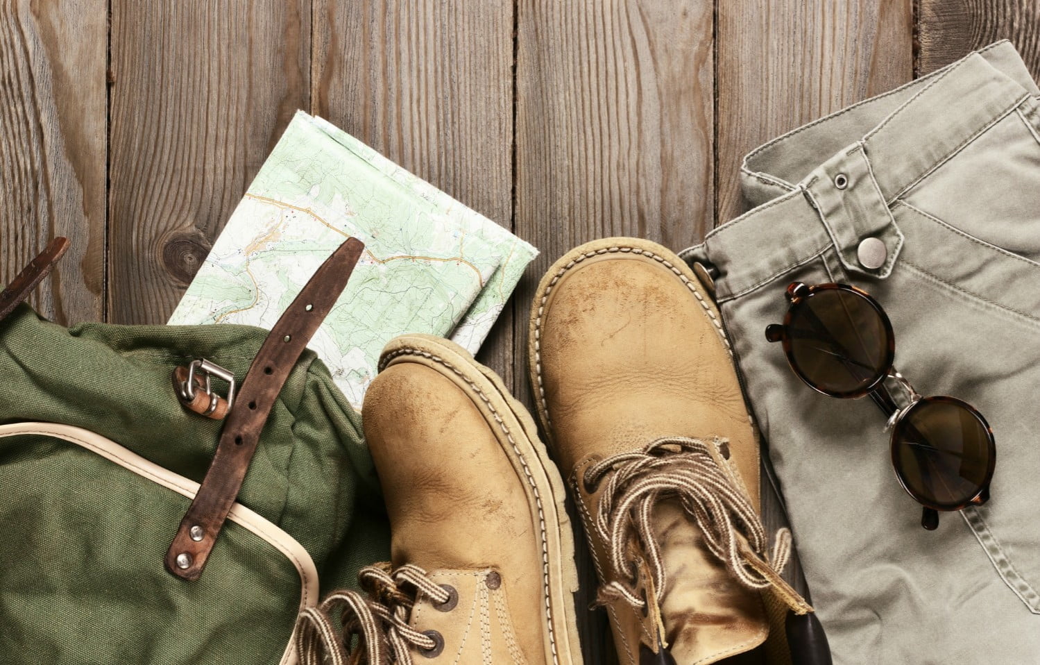 Travel accessories set on wooden background: old hiking leather boots, pants, backpack, map and sunglasses | Marion Tallgrass Trail